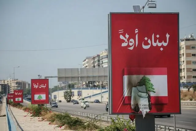 سيارات تمر قرب لافتات “لبنان أولاً” على طريق مطار بيروت، بعدما رفض حزب الله الاتفاق الإطاري بين لبنان وإسرائيل واتهم الحكومة بتقويض السيادة اللبنانية.