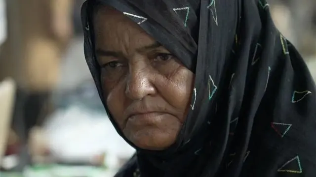 لقطة قريبة لامرأة ترتدي حجاباً أسود مزيناً بمثلثات متعددة الألوان.