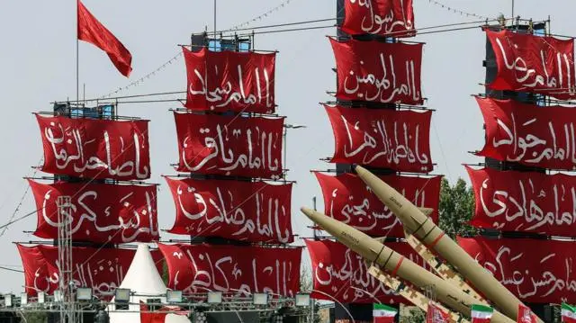سفن ذات أشرعة حمراء وكتابات باللغة الفارسية، وأمامها صواريخ خلال احتفال عسكري في إيران.