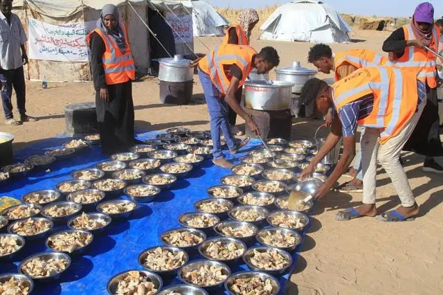 متطوعون سودانيون بإعداد وجبات مجانية للنازحين من مدينة الفاشر في مخيم العفاض للنازحين بمدينة الضبّة شمال السودان